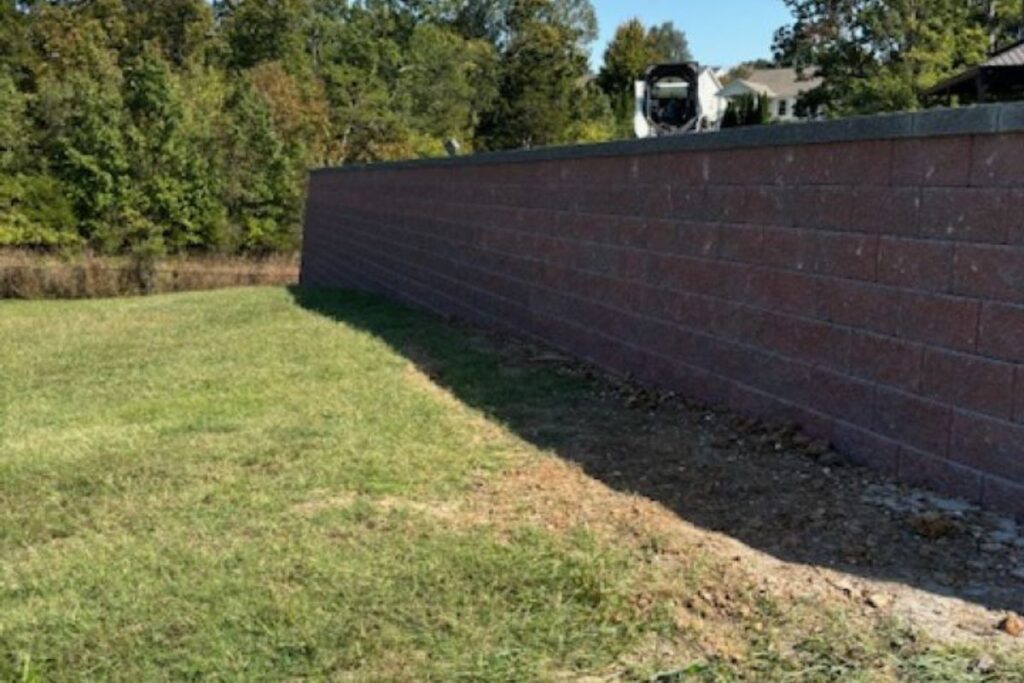 Drainage system installation behind a retaining wall in St. Louis with gravel backfill, perforated pipe, and filter fabric to prevent soil pressure and leaning
