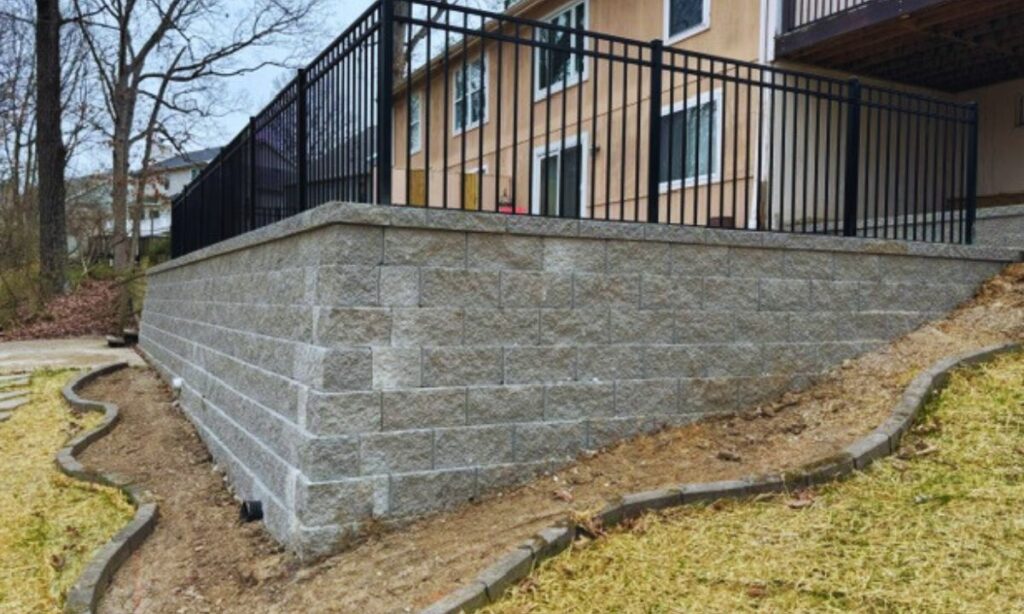 Modern concrete block retaining wall with black railing, built by Retaining Wall & Paving Solutions in a St. Louis residential yard