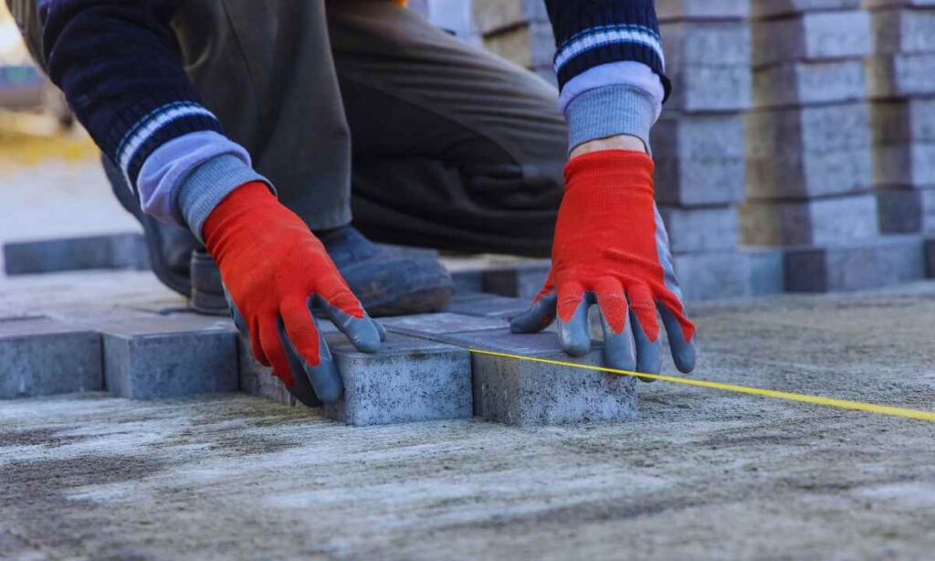 contractor’s gloved hands laying concrete pavers with a measuring string during a backyard hardscaping project