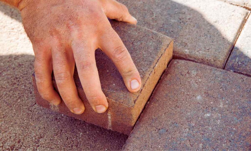 worker’s hand placing a concrete paver into sand base during a patio installation in St. Louis, Missouri.