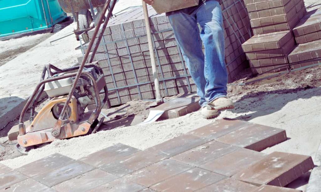 Construction worker using compactor to install concrete pavers on a driveway in St. Louis, showing the setup process for long-term ROI.
