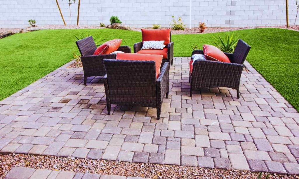 A backyard patio in St. Louis featuring a clean paver surface with wicker chairs and red cushions, showing how regular maintenance keeps outdoor spaces inviting and free of stains.