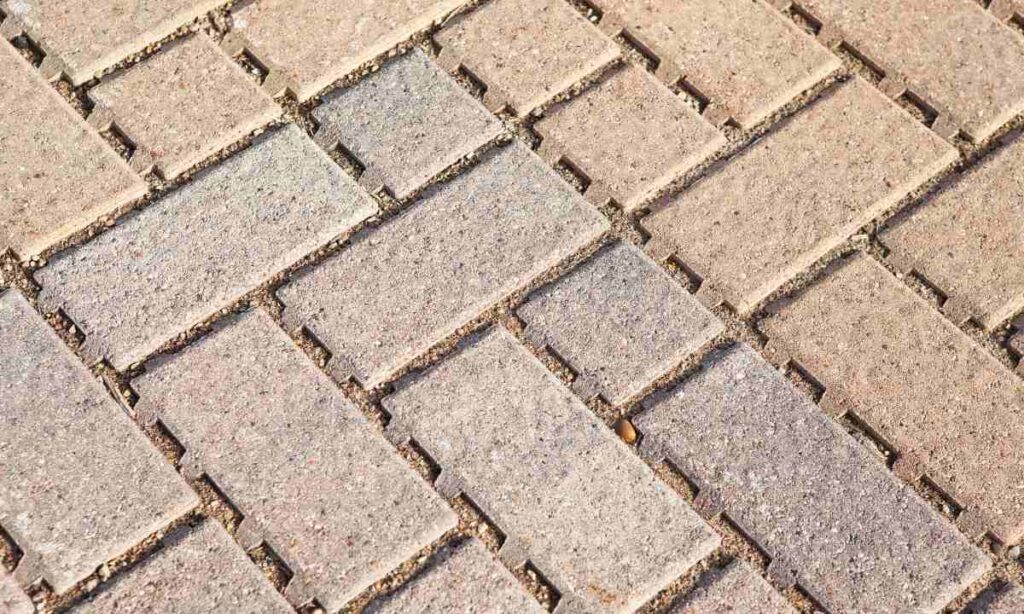 Detailed view of interlocking concrete pavers with visible joint gaps, highlighting the need for polymeric sand to stabilize the surface and prevent weed growth.