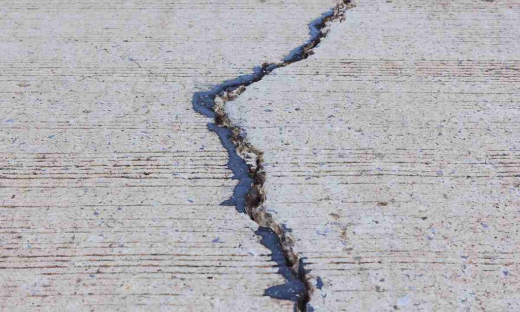 Wide crack running through a concrete driveway slab, showing the damage caused by expansive clay soil movement in St. Louis when proper base preparation and drainage are ignored.