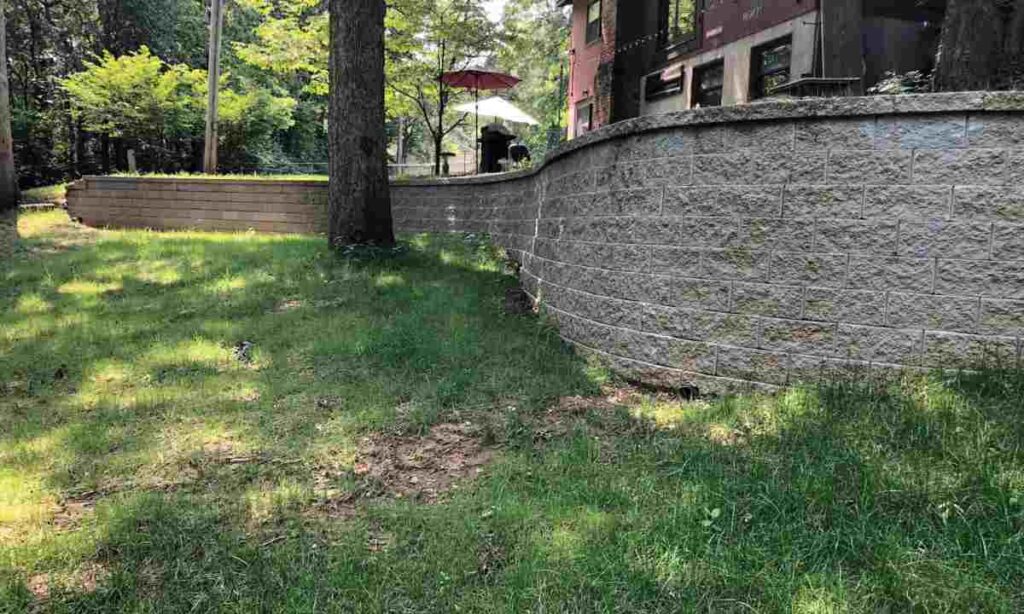 curved segmental retaining wall holding back sloped soil near residential home