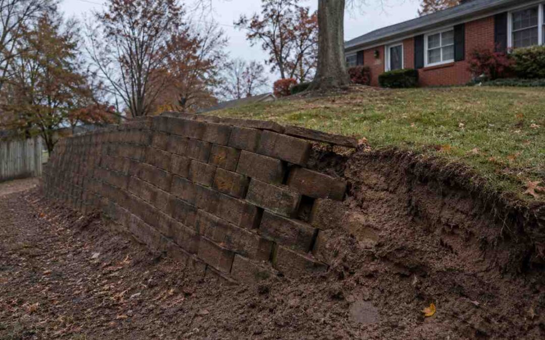 Concrete block retaining wall leaning forward with displaced blocks and soil erosion at a St. Louis residential property line
