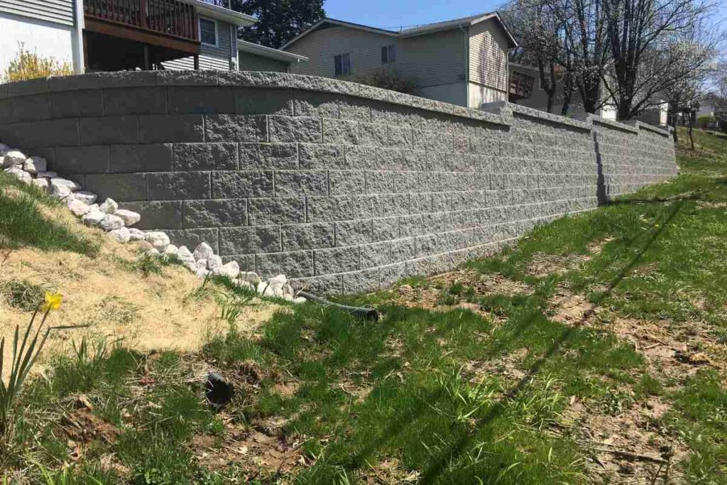 Concrete segmental retaining wall at permit-required height near a residential property line in St. Louis with measuring tape showing scale